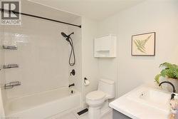 Full bathroom featuring a tub/shower combination with matte black fixtures, white subway tile surround, white toilet, and a vanity with an integrated sink and light-colored countertop - 