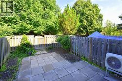 Paved patio area with a wooden privacy fence and mature trees - 