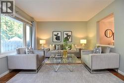 Living area featuring a large picture window, a wall cutout to an adjoining room, light-toned walls, and wood-finish flooring - 