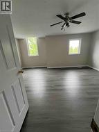 Spacious room featuring wood-finish flooring, two windows, and a ceiling fan with integrated lighting - 