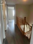 Hallway featuring dark wood-finish flooring, light-toned walls, and a natural wood staircase with balusters - 