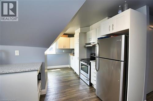 Kitchen featuring stainless steel appliances, white cabinetry, wood-finish flooring, light-toned countertops, and a built-in electric range with exhaust hood - 242 James Street S, Hamilton, ON 