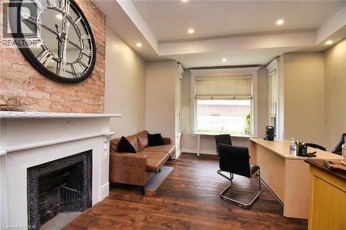 Exposed brick accent wall featuring a decorative fireplace with a white mantel, wood-finish flooring, recessed lighting, and bay windows - 242 James Street S, Hamilton, ON 