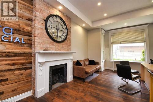 Exposed brick wall featuring a decorative fireplace with a white mantel, complemented by wood-finish flooring and recessed lighting - 242 James Street S, Hamilton, ON 