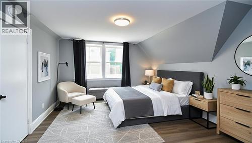 Spacious room featuring sloped ceilings, two large windows with dark drapery, wood-finish flooring, and a flush-mount ceiling light fixture - 242 James Street S, Hamilton, ON 