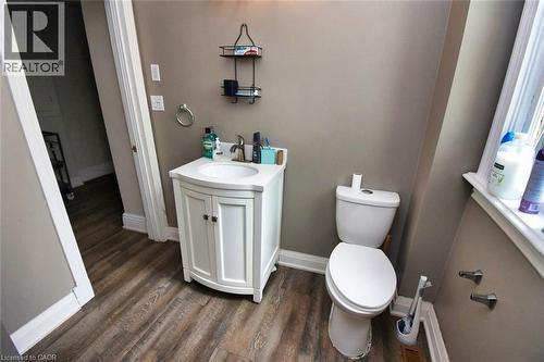 Bathroom featuring wood-finish flooring, a white vanity with an integrated sink, a white toilet, and a window with white trim - 242 James Street S, Hamilton, ON 