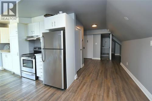 Kitchenette featuring a stainless steel refrigerator and range, white cabinetry, light countertops, and wood-finish flooring - 242 James Street S, Hamilton, ON 