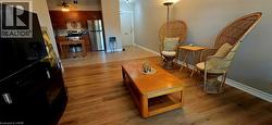 Open-concept living space featuring wood-finish flooring, a kitchen with dark wood cabinetry, a stainless steel refrigerator, and a tiled backsplash - 