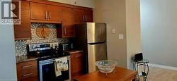 Kitchen featuring wood-finish cabinetry, stainless steel appliances, a mosaic tile backsplash, and dark countertops - 