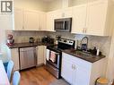 Corner kitchen featuring white upper and lower cabinetry, dark countertops, a stainless steel dishwasher, a stainless steel range oven, and wood-finish flooring - 207 Charlton Avenue W, Hamilton, ON 