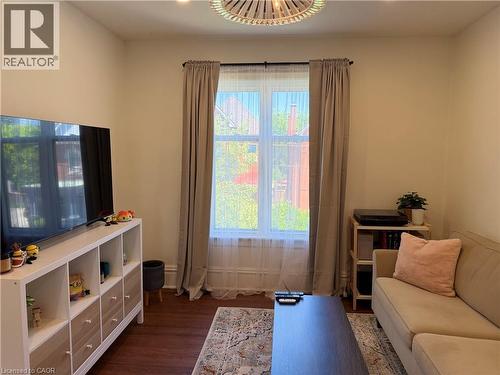 Living area featuring wood-finish flooring, a large window, a built-in media console, a ceiling light fixture, and neutral wall tones - 207 Charlton Avenue W, Hamilton, ON 