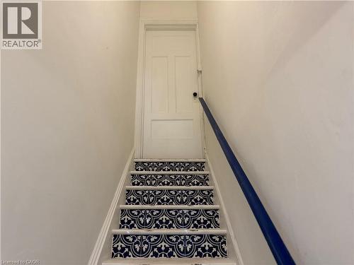 Staircase with contrasting patterned risers and a dark blue handrail - 207 Charlton Avenue W, Hamilton, ON 