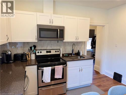 Kitchen featuring white shaker-style cabinetry, dark granite-look countertops, and a gray stone-look backsplash - 207 Charlton Avenue W, Hamilton, ON 