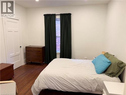 Room featuring wood-finish flooring, a window with dark curtain panels, and a white paneled door - 207 Charlton Avenue W, Hamilton, ON 