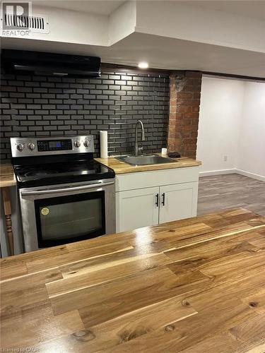 Stainless steel electric range, dark brick-patterned tile backsplash, wood-finish countertops, stainless steel sink with gooseneck faucet, and white base cabinetry - 207 Charlton Avenue W, Hamilton, ON 