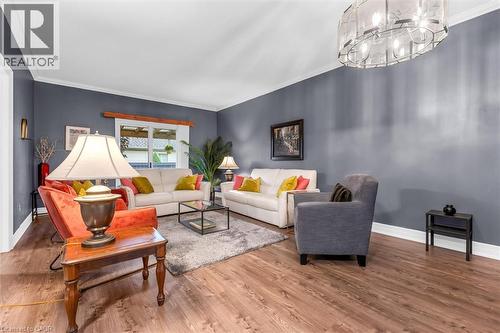 Spacious living area featuring wood-finish flooring, a contemporary chandelier, crown molding, and a large window - 149 Silverbirch Boulevard, Hamilton, ON 