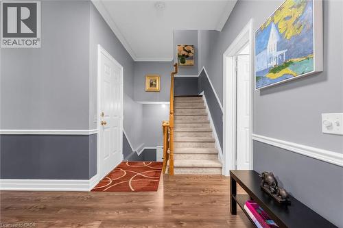 Entryway featuring wood-finish flooring, a white paneled entry door, and a carpeted staircase with wood handrails - 149 Silverbirch Boulevard, Hamilton, ON 