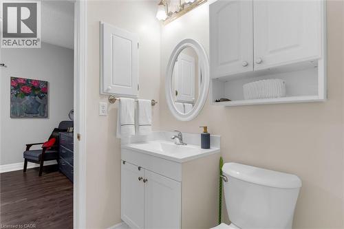 Powder room featuring a white vanity with integrated sink, an oval mirror, and a wall-mounted cabinet with open shelving - 149 Silverbirch Boulevard, Hamilton, ON 