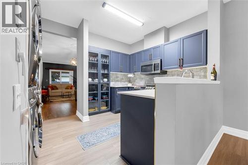 Contemporary kitchen featuring blue cabinetry, light-toned wood-finish flooring, and stainless steel appliances - 149 Silverbirch Boulevard, Hamilton, ON 
