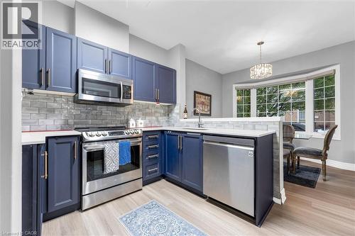 Contemporary kitchen featuring blue shaker-style cabinetry, stainless steel appliances, light wood-finish flooring, white countertops, and a gray subway tile backsplash - 149 Silverbirch Boulevard, Hamilton, ON 