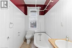 Bathroom featuring white paneled wainscoting, a standalone bathtub with an overhead shower, and a wood-finish vanity with an integrated sink - 