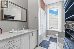 Bathroom featuring a single vanity with white cabinetry, a large framed mirror, a separate shower/tub combination with a shower curtain, a window with natural light, and tiled flooring - 