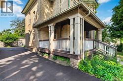 Brick-clad residence featuring a covered front porch with substantial columns, white balusters, and a dark-stained railing - 
