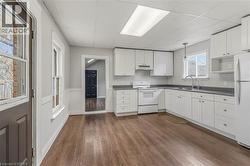 Modern kitchen featuring white cabinetry, dark wood-finish flooring, a stainless steel sink, and white appliances - 