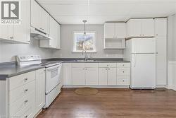 Spacious kitchen featuring white cabinetry, dark countertops, wood-finish flooring, a stainless steel sink with a gooseneck faucet, and a pendant light fixture - 