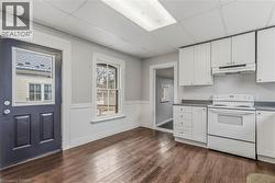 Kitchen area featuring wood-finish flooring, white cabinetry, a white electric range with overhead exhaust, and a window with white trim - 