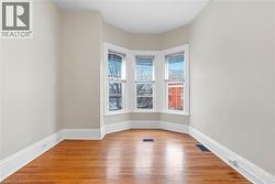 Bay window with multiple panes, hardwood flooring, light-toned walls, white trim, and baseboard registers - 