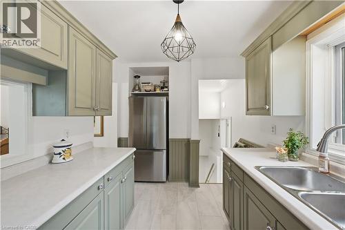 Galley kitchen featuring light green cabinetry, light countertops, wood-finish flooring, a stainless steel refrigerator, and a double basin sink - 81 Vale Avenue, St. Catharines, ON 
