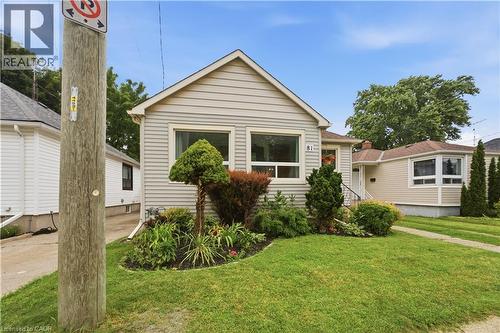 Light-toned siding exterior with multiple windows, a manicured lawn, and established front garden beds - 81 Vale Avenue, St. Catharines, ON 