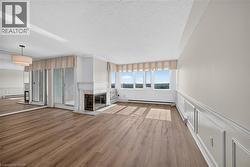 Expansive living area featuring wood-finish flooring, a white mantel fireplace with a dark-toned firebox, and large windows offering broad exterior scenery - 