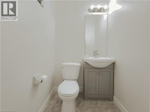 Powder room featuring a white toilet, gray vanity with cabinet storage, integrated white basin, and wall-mounted mirror with overhead lighting - 78 Colton Circle, Kitchener, ON 