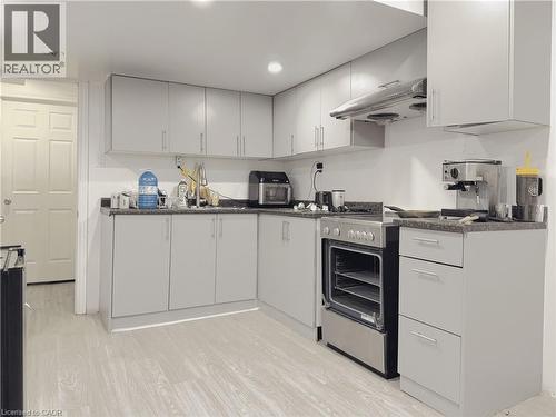 Kitchen featuring light gray cabinetry, stainless steel range with overhead ventilation, dark stone-look countertops, and wood-finish flooring - 78 Colton Circle, Kitchener, ON 