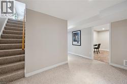 Carpeted staircase with wooden handrail, leading to a hallway with neutral walls and white trim - 