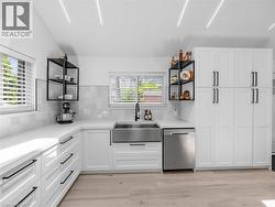 Modern kitchen featuring white shaker cabinetry with black hardware, an undermount stainless steel farmhouse sink, and light wood-finish flooring - 