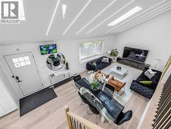 Open-concept living and dining area featuring light wood-finish flooring, a vaulted ceiling with integrated linear lighting, and a large skylight - 