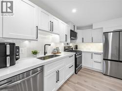Lower level kitchen featuring white shaker cabinetry, stainless steel appliances, light-toned wood-finish flooring, white countertops, and a subway tile backsplash - 