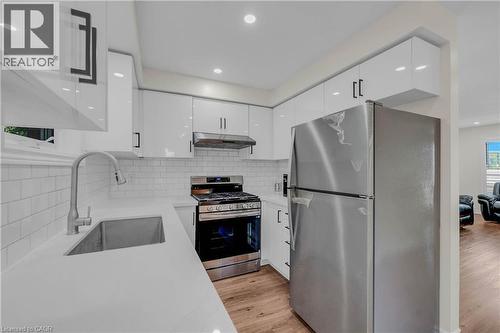 Contemporary kitchen featuring white shaker-style cabinetry, a subway tile backsplash, stainless steel appliances, a stainless steel sink with a pull-down faucet, and wood-finish flooring - 191 Stirling Macgregor Drive, Cambridge, ON 