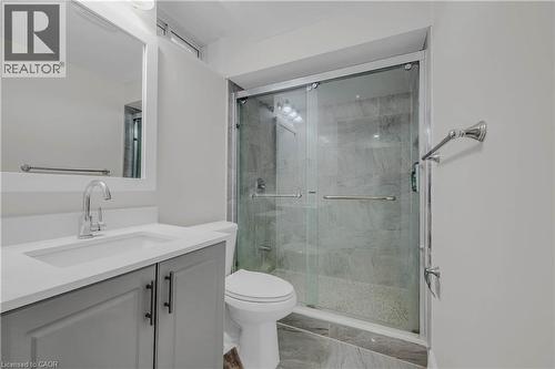 Contemporary bathroom featuring a glass-enclosed shower with stone-finish tile, a light gray vanity with a built-in sink, a wall-mounted mirror, and tile flooring - 191 Stirling Macgregor Drive, Cambridge, ON 