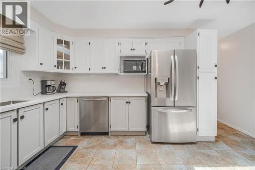 Kitchen featuring white cabinetry with dark hardware, a stainless steel refrigerator, stainless steel dishwasher, and built-in microwave - 23 Millpond Place, Mountain, ON 