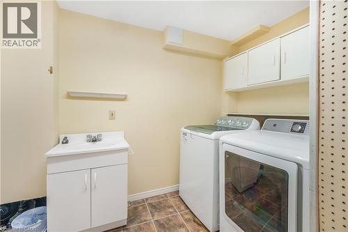 Dedicated laundry area featuring a utility sink with a white cabinet, overhead cabinetry for storage, and durable tile flooring - 23 Millpond Place, Mountain, ON 