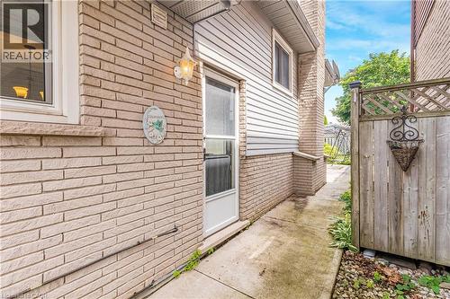 Exterior side entrance featuring light brick siding, white vinyl siding, a side door, and a concrete pathway - 23 Millpond Place, Mountain, ON 