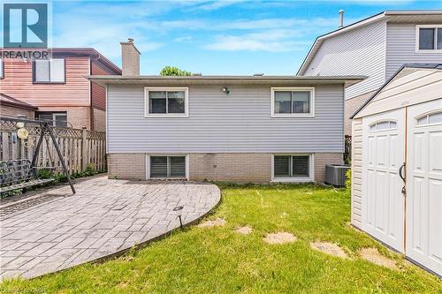 Rear exterior featuring light grey siding with white trim windows, a brick foundation, and a central chimney - 23 Millpond Place, Mountain, ON 