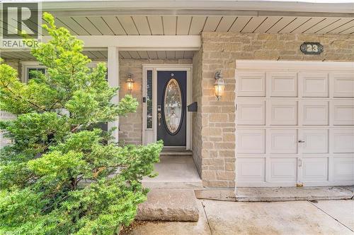 Stone facade entry with covered porch featuring a dark wood-finish door with oval glass insert, decorative exterior lighting, and an attached single-car garage - 23 Millpond Place, Mountain, ON 