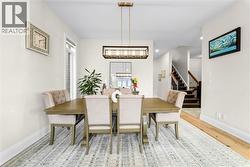 Formal dining area featuring a linear chandelier, light wood-finish flooring, and a stairway with dark wood treads and a wood railing - 