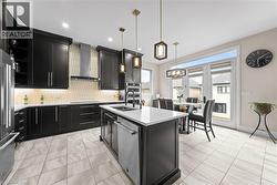 Modern kitchen featuring dark cabinetry, stainless steel appliances, a center island with sink, stylish pendant lighting, and light-toned tile flooring - 