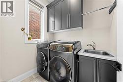 Laundry area featuring dark gray cabinetry, a utility sink with a chrome faucet, a wall-mounted drying rack, and a window with white trim - 